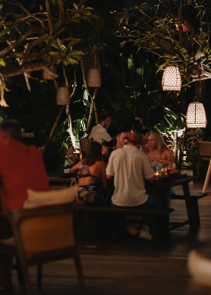 Guests dining at Kaban Bali restaurant and bar under bamboo lights in lush garden setting